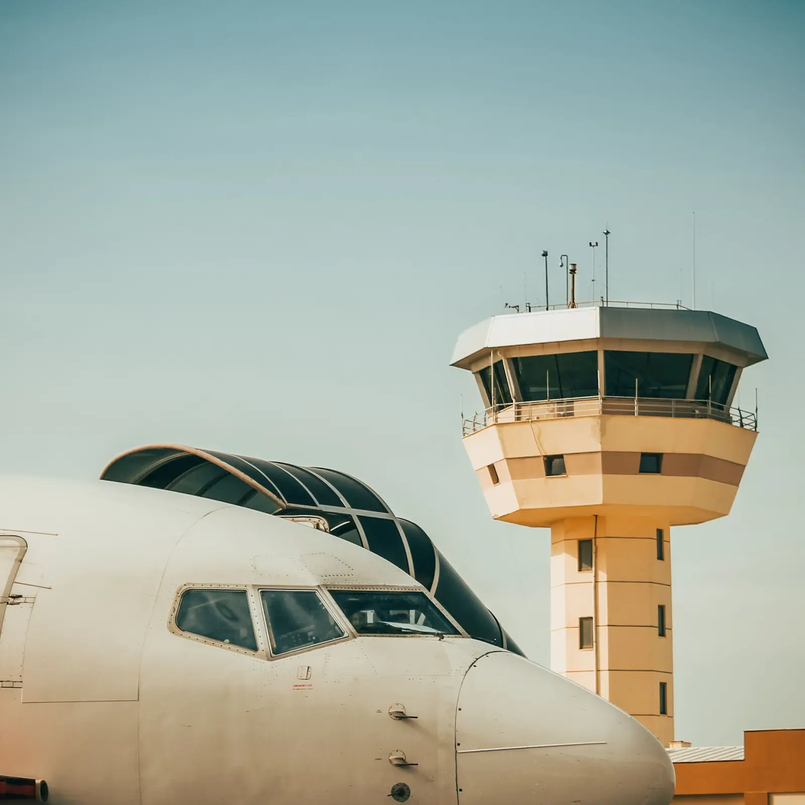 The nose of a passenger aircraft in front of a control tower.