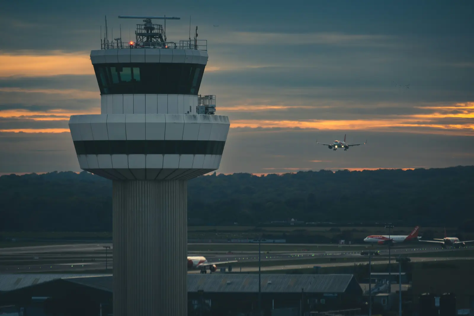 A control tower at dusk, with an easyJet aircraft in the air and others on the ground.